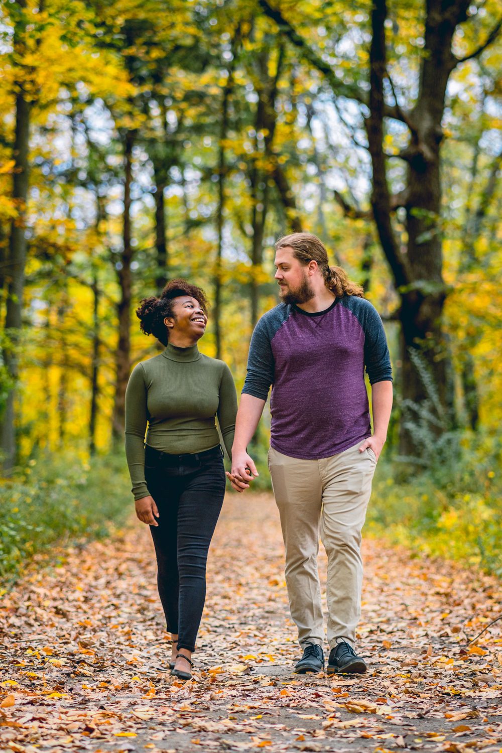 A couple walking hand in hand down a leaf-covered forest path