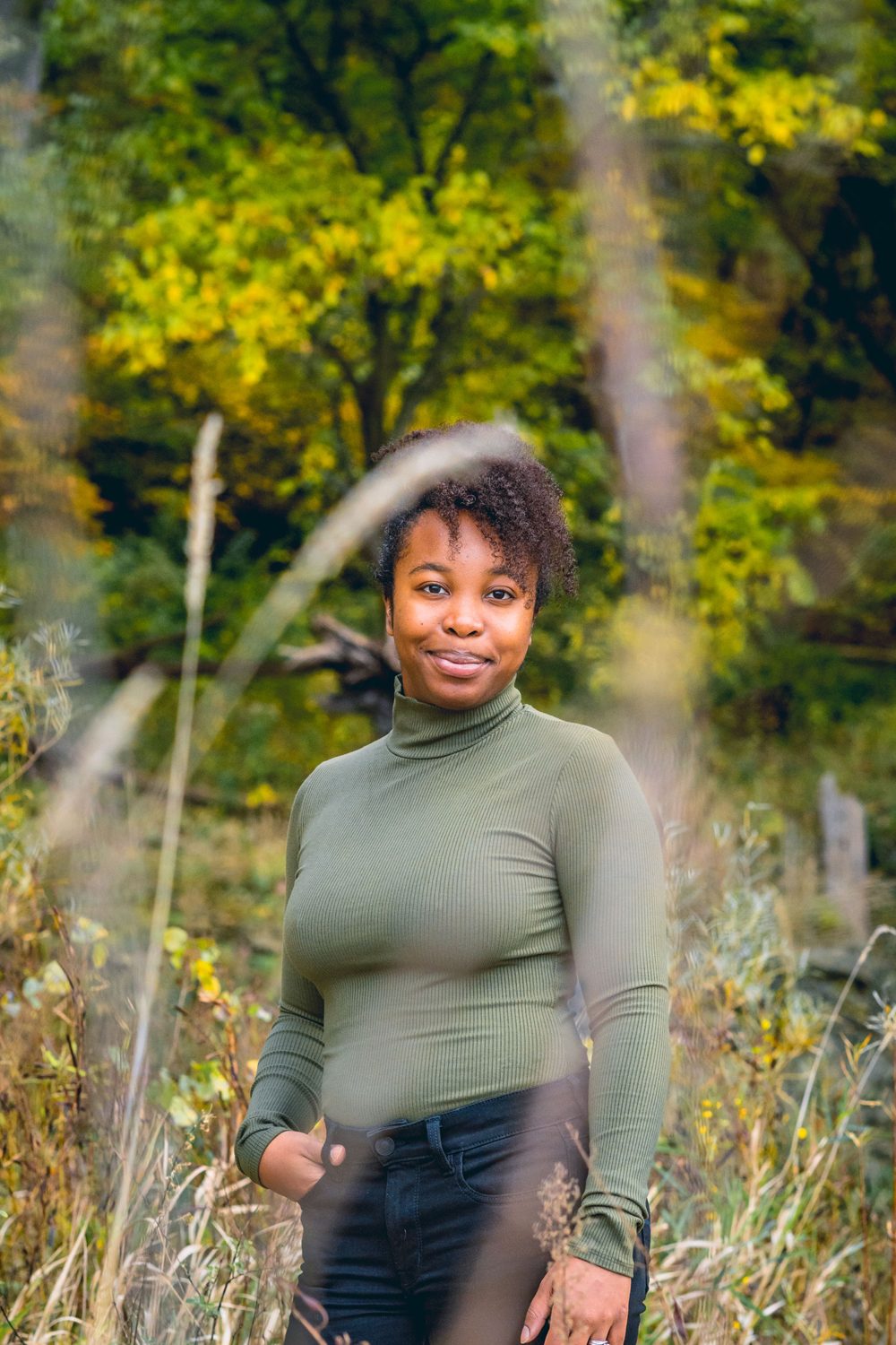 A woman in a green turtleneck standing in tall autumn grass